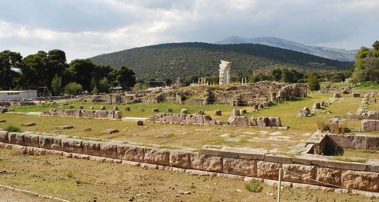 Site archéologique avec des pierres anciennes éparses et des collines au loin.
