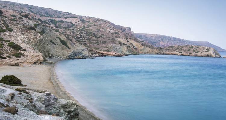 Een serene strand met helder blauw water en rotsachtige kliffen.