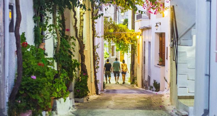Smalle steeg omzoomd met kleurrijke bloemen en wandelende mensen.