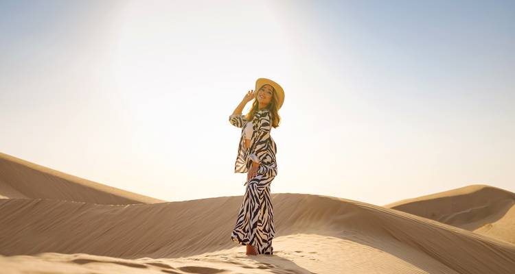Woman in patterned dress standing on sand dunes.
