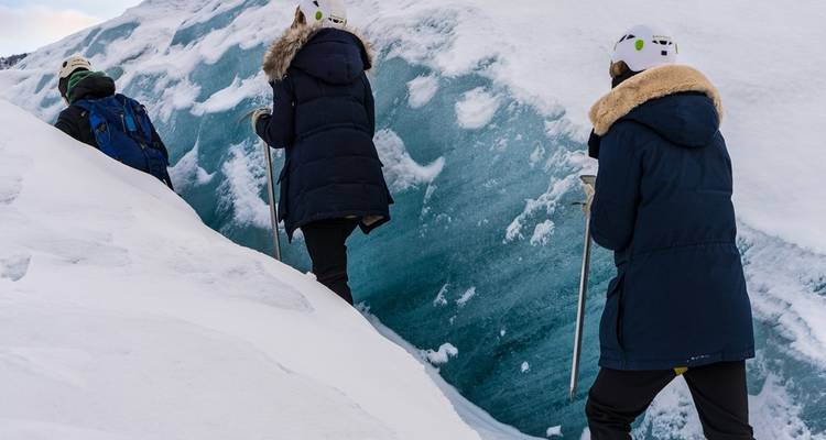 Trois personnes faisant de la randonnée sur un glacier, portant des équipements d'hiver en Islande.