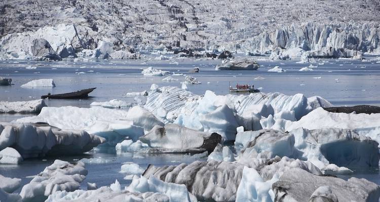 Icebergs flottant sur un lac glaciaire avec des bateaux visibles.