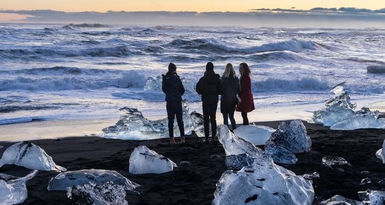 Des personnes explorant une plage glacée avec des blocs de glace provenant de glaciers, Islande.