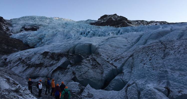 Groupe de personnes explorant un grand glacier avec des formations de glace bleu profond.