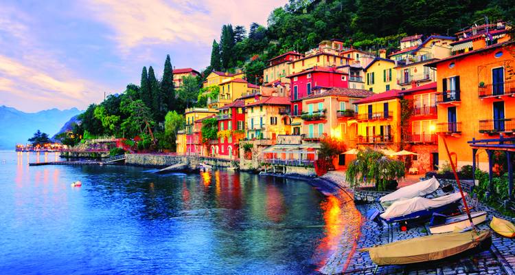 Village pittoresque au bord du lac avec des maisons en terrasses illuminées au crépuscule contre les eaux calmes et bleues.