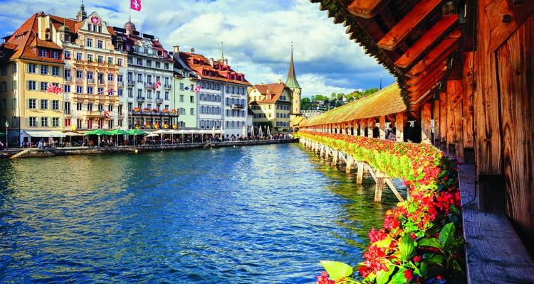 Le Pont de la Chapelle de Lucerne, orné de fleurs rouges, s'étend sur la rivière Reuss à côté de bâtiments historiques.