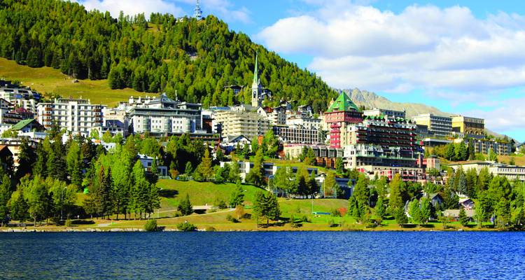 La station de villégiature alpine haut de gamme de St-Moritz, nichée entre des pentes boisées et un lac bleu.