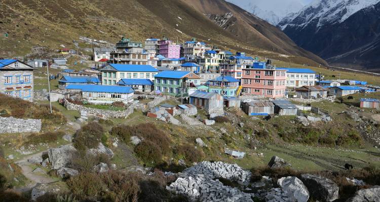 Ein abgelegenes Himalaya-Dorf mit farbenfrohen Wellblechdächern liegt in einem Tal unter schneebedeckten Gipfeln.