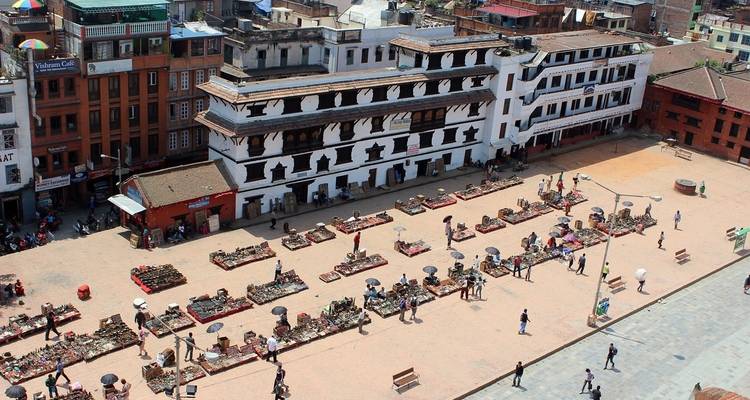 Place de ville avec étals de marché et gens épars.