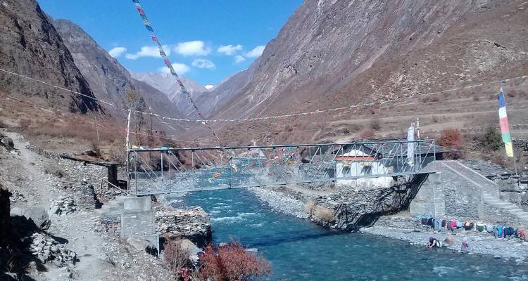 Pont suspendu avec drapeaux de prière au-dessus d'une rivière dans une vallée.