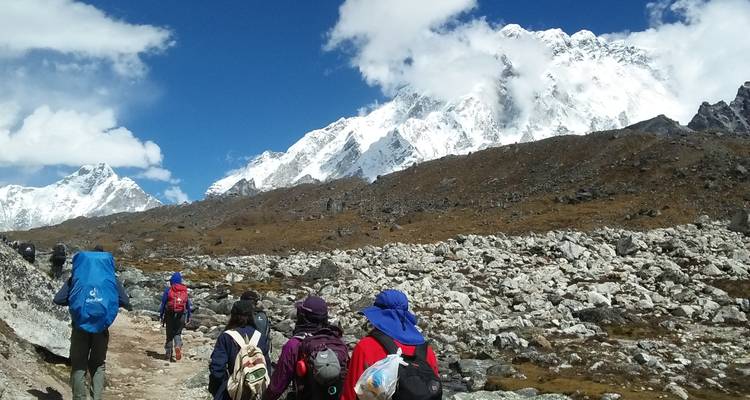 Randonneurs marchant sur un sentier rocheux avec des montagnes enneigées devant eux.