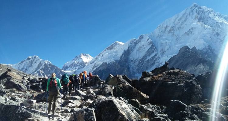 Groupe de randonneurs gravissant un sentier de montagne sous un ciel bleu dégagé.