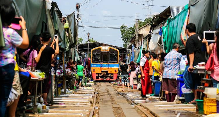 Train traveling through a lively market, with vendors on either side.