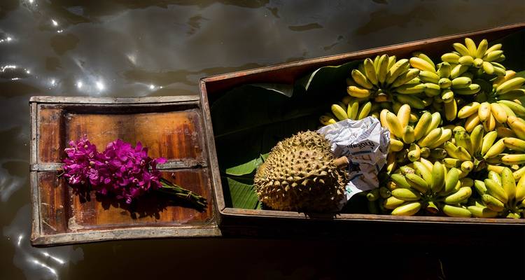 Arrangement of bananas, flowers, and durian in a wooden boat on the water.