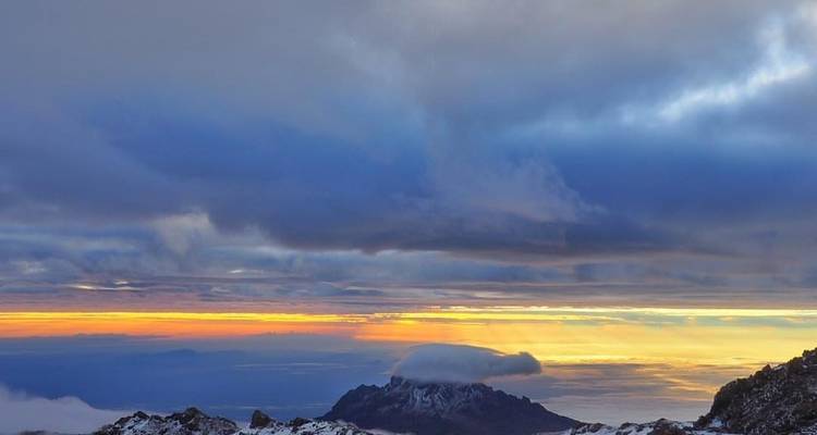 A mountain peak under a cloudy sky during sunrise.