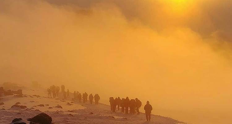 People hiking in snow with a glowing sun and fog in the background.