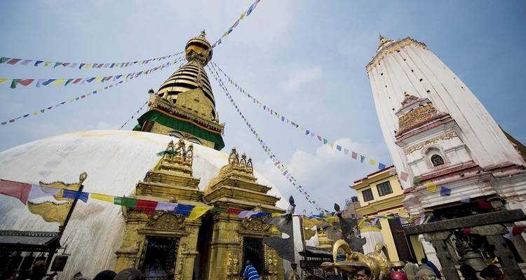 Ikonische Stupa mit Gebetsfahnen und Menschenmengen von Besuchern unter blauem Himmel.
