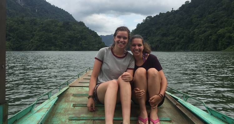 Dos personas sentadas en el borde de un barco en un lago.