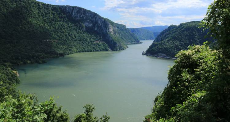 Un canyon fluvial pittoresque bordé de collines verdoyantes sous un ciel nuageux.