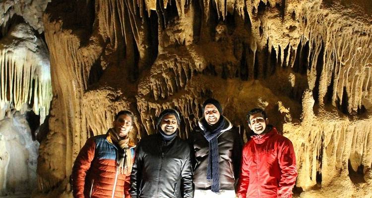 Quatre personnes debout dans une grotte faiblement éclairée avec des stalactites.