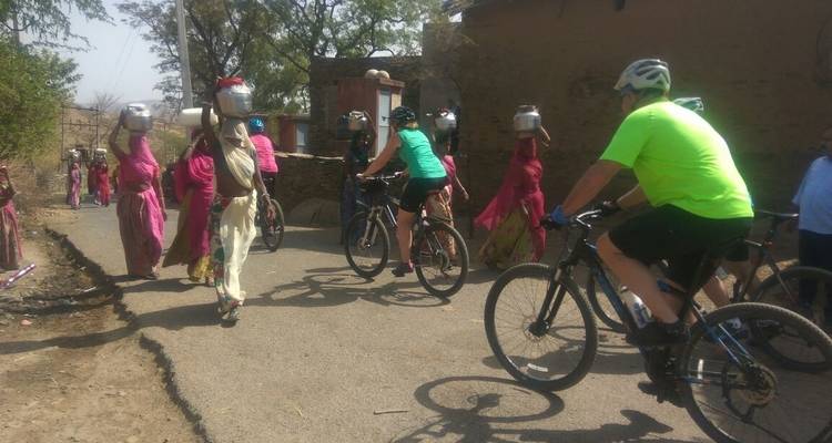 Cyclists passing villagers carrying pots on a rural road.