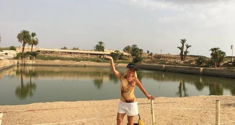 A person posing by a water body with desert landscape in the background.