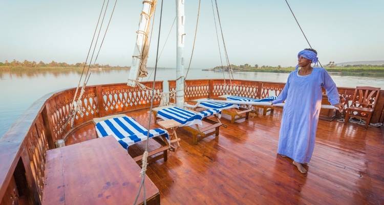 Dek van een boot met ligstoelen en een persoon in traditionele kleding.