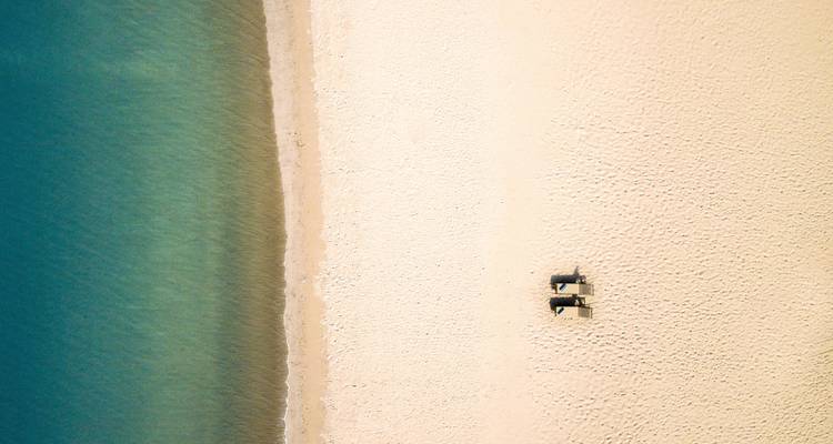 Luchtfoto van een zandstrand met helderblauw water.