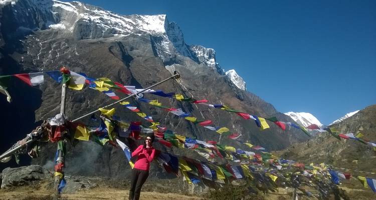 Een persoon die tussen kleurrijke gebedsvlaggen staat met bergen op de achtergrond.