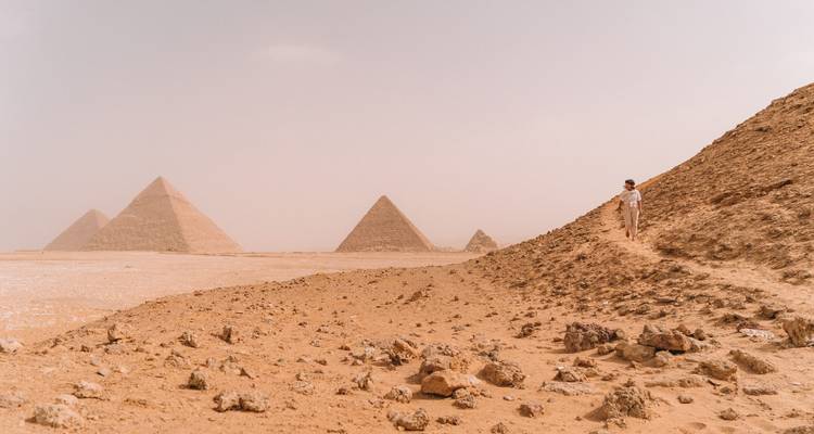 Staubige Sicht auf Pyramiden mit einer Person auf einer Düne.