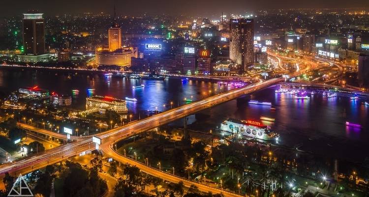 A night view of a brightly lit city with a river running through it and high-rise buildings in the background.
