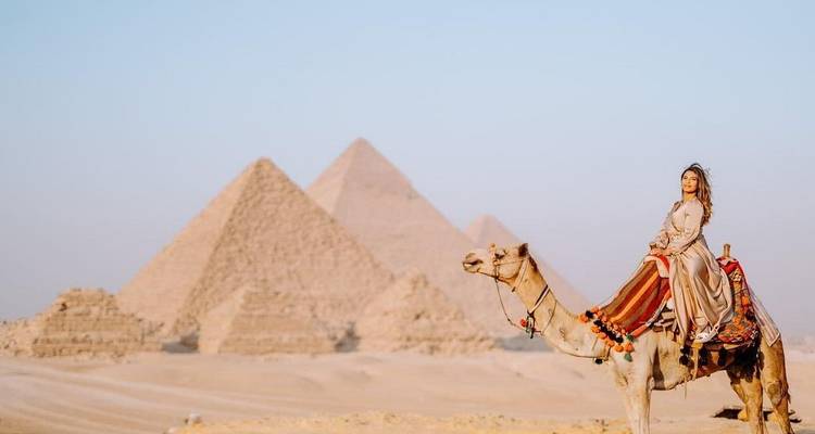 Woman riding a camel in front of Giza pyramids with clear sky.