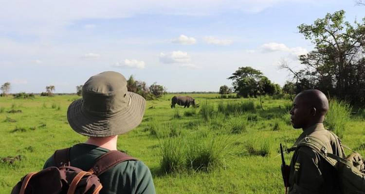 Twee mensen die een neushoorn observeren in een grasrijke safari-omgeving.