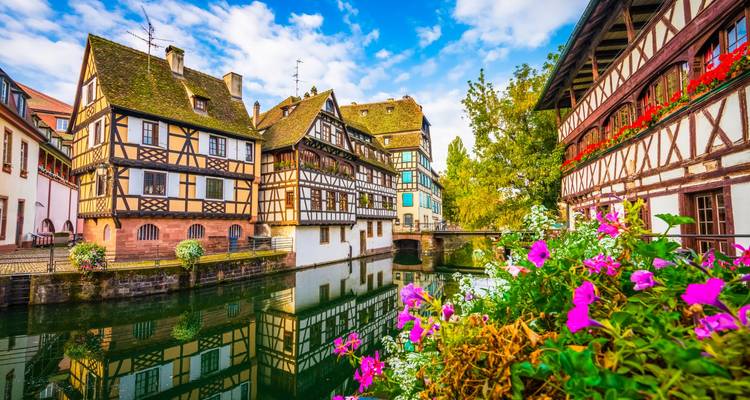 Maisons à colombages pittoresques reflétées dans un canal tranquille avec des fleurs colorées dans la Petite France de Strasbourg