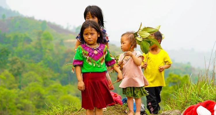 Quatre enfants de minorités ethniques se tiennent sur une colline herbeuse avec des montagnes douces au loin.