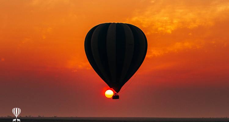 Silhouet van een heteluchtballon die voor de ondergaande zon langs gaat tegen een vuurrood oranje lucht