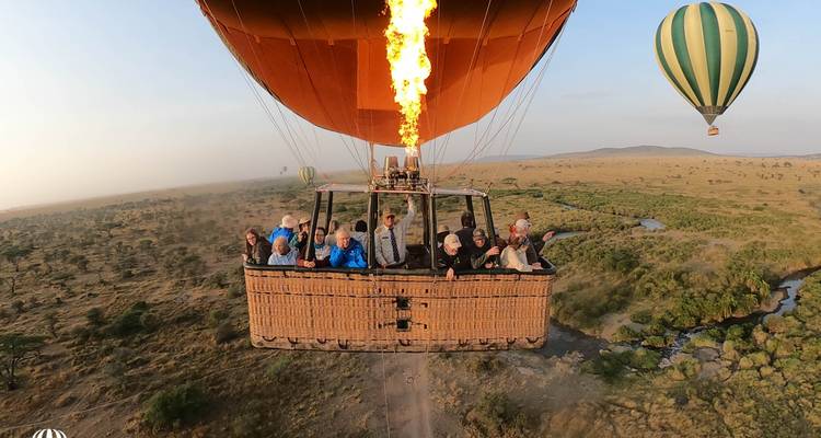 Mand vol reizigers stijgt op in een gloeiende heteluchtballon boven de Serengeti-vlaktes terwijl een ander ballon in de buurt zweeft