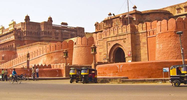 Historic red sandstone fort with people and tuk-tuks nearby.