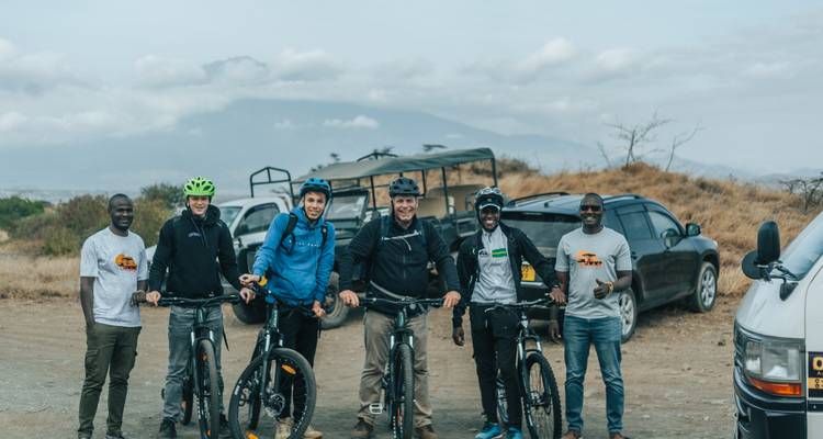 Gruppe von Radfahrern, die mit einem Safari-Fahrzeug auf einer unbefestigten Straße posieren.