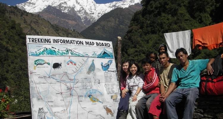 Groupe de randonneurs assis près d'une carte de randonnée avec des montagnes en arrière-plan.