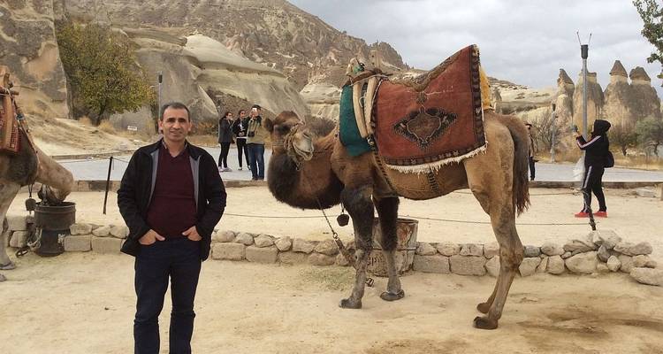 Man posing with a camel in a rocky landscape.