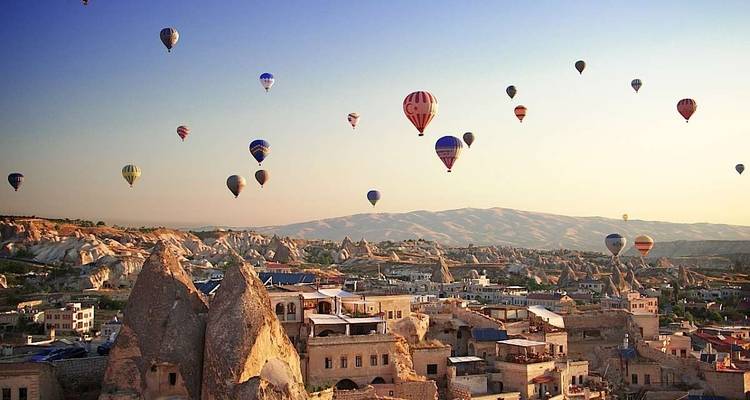 Hot air balloons over a unique rocky landscape with a town below.
