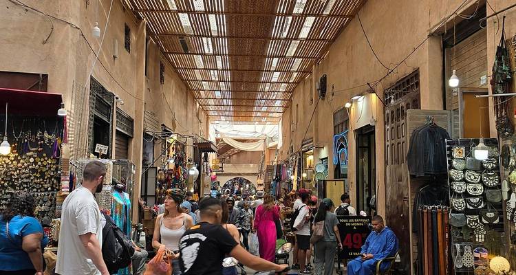 Lebendiger überdachter Marktgang voller Einkäufer, Stoff- und Souvenirstände in Marrakesch.