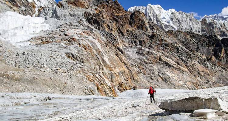 Montañero en solitario trekking a través de un glaciar accidentado bajo acantilados imponentes.