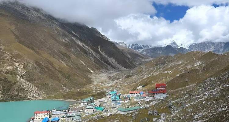 Asentamiento de gran altitud junto a un lago glacial color turquesa rodeado de picos áridos.