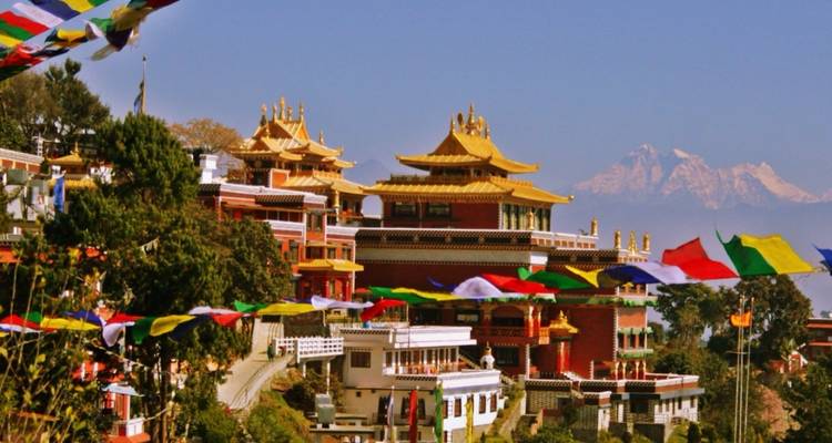 Bunte Gebetsfahnen wehen über einem Kloster mit majestätischen Bergen im Hintergrund.
