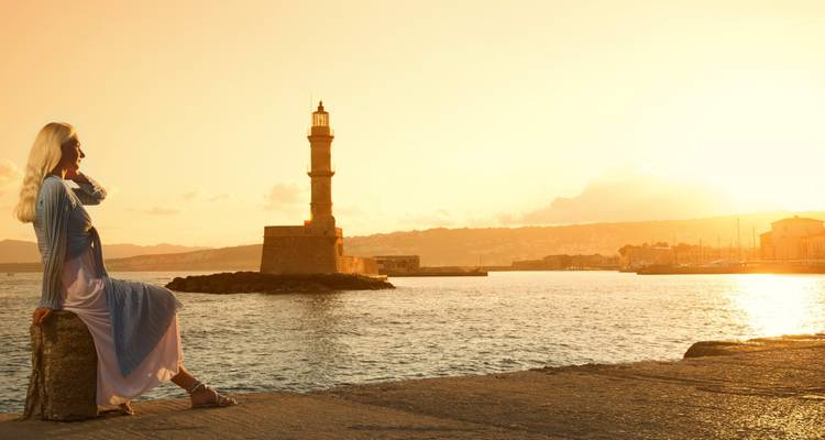 Woman sitting near a lighthouse at sunset.