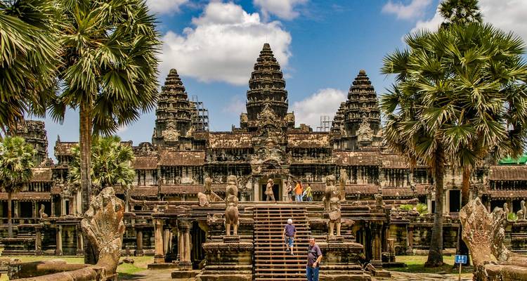 Templo de Angkor Wat con visitantes en las escaleras, rodeado de palmeras.