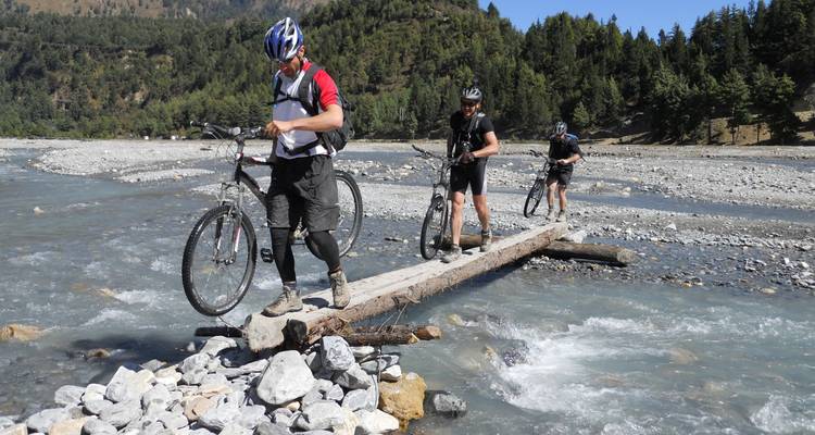 Cyclists crossing a river using a log bridge.