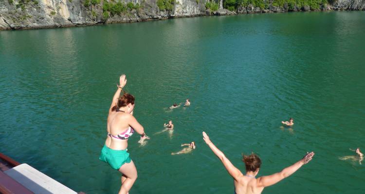 People jumping into the waters of Halong Bay with limestone cliffs in the background.